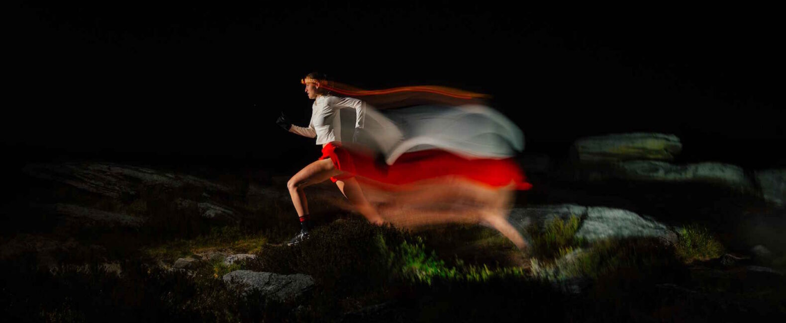 An Athletic Woman Wearing A Headlamp Runs Through A Rocky Terrain At Night