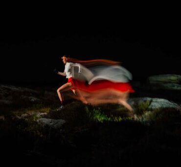 An Athletic Woman Wearing A Headlamp Runs Through A Rocky Terrain At Night