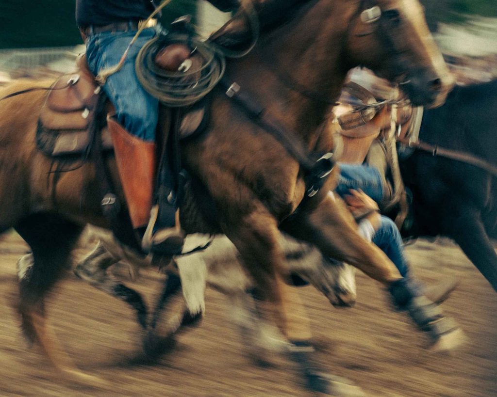 A Motion-blurred Action Shot Captures A Rider On A Galloping Brown Horse